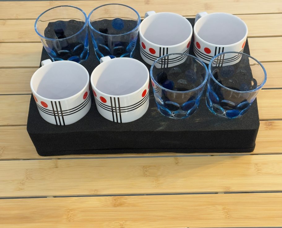 Tassen und Becher Sechs Gläser auf einem Tisch mit einem schwarzen Untersetzer, einige mit blauen Details.