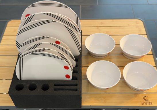 Geschirrständer mit gestapelten Tellern und Schalen auf einem Holzbrett.