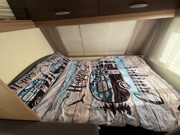 Doppelbett Bett mit buntem Bettbezug in einem kleinen Raum, Licht fällt durch das Fenster.