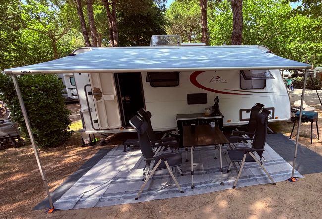 Ein Wohnwagen unter einem Sonnensegel mit Stühlen und Tisch im Freien.