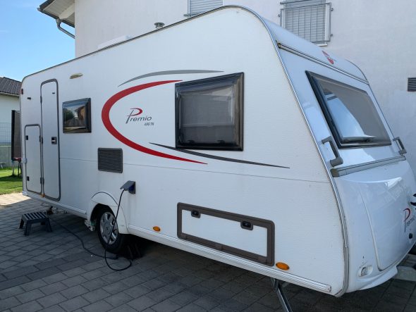 Wohnwagen Weißer Wohnwagen mit roten Akzenten, parkt auf einem gepflasterten Platz.