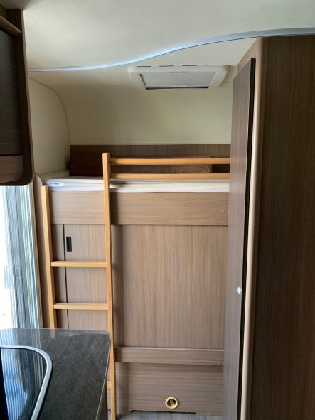 Stockbett Hochbett in einem Wohnmobil, mit Holzleiter und angrenzendem Schrank.
